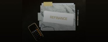 The word "refinance" written on a piece of paper, right next to a pen and a calculator.