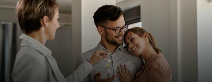 A young couple receiving the keys of their new home from a real estate agent