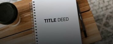 A notebook with the words "Title Deed" on the cover, laying on top of a desk next to a pen and cup of coffee.